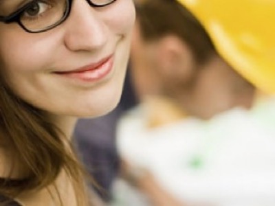 women smiling at camera with man in a hard hat in the background featured