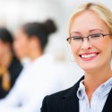 Blonde office woman with glasses smiling with office co workers in background