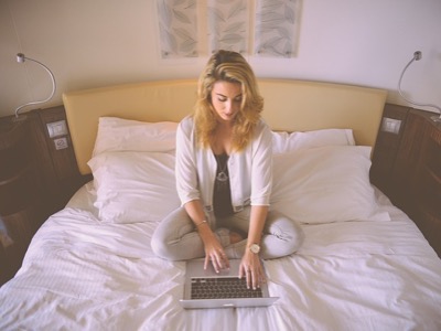 Blonde woman sitting on her bed whilst working on her laptop