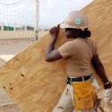 female apprentice construction worker carrying plank of wood featured