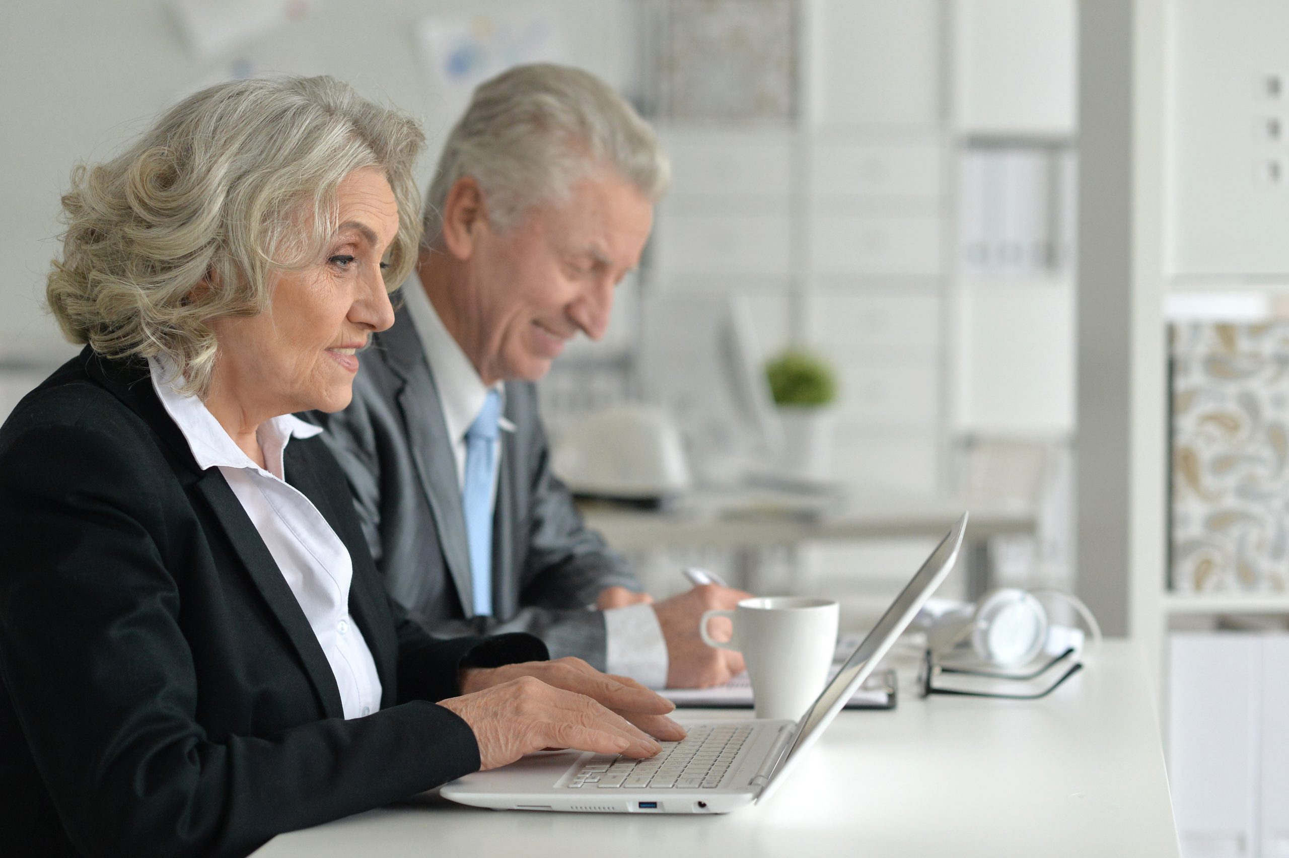 Older business man and woman on laptop, supporting older workers