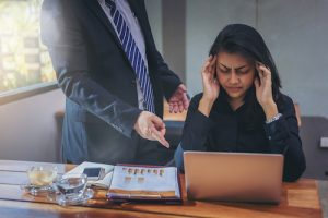 Toxic boss blaming woman for her work in the office. Woman has a headache