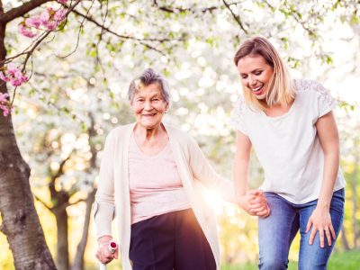 Elderly grandmother with crutch and granddaughter in spring nature, carer