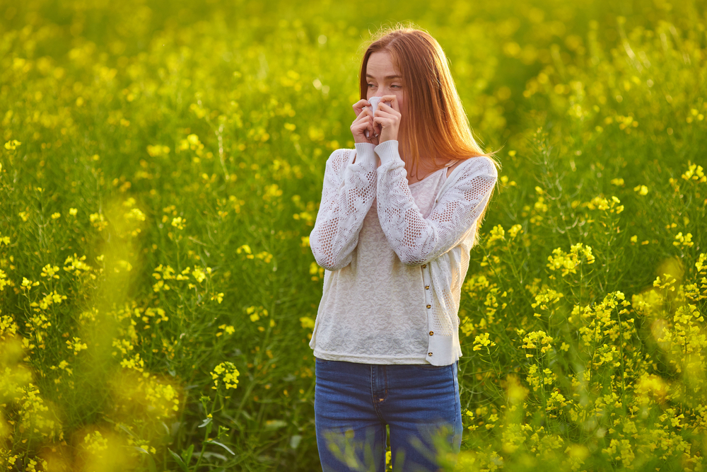 woman with hayfever standing in a field of flowers, allergies