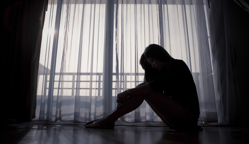 Sad woman sitting alone near window, human trafficking