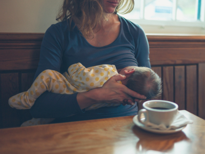 A young mother is breastfeeding her baby in a cafe while she is having a coffee