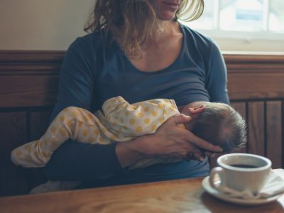 A young mother is breastfeeding her baby in a cafe while she is having a coffee