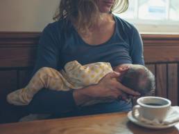 A young mother is breastfeeding her baby in a cafe while she is having a coffee