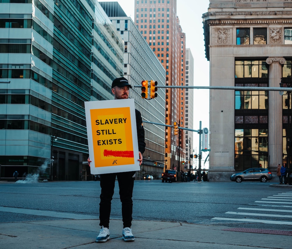 man holding a sign in the street, saying slavery still exists