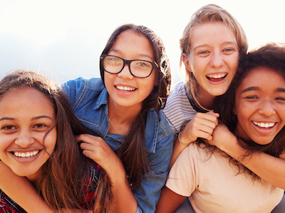 Four teenage girls having fun piggybacking outdoors, Reach Next Generation summit, empowerment