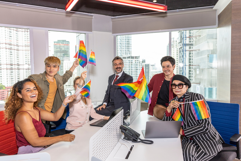 Business office workers from different ethnicities express support for self determination in LGBT. Business people showing LGBT flags in an office. Business people support Gender Equality