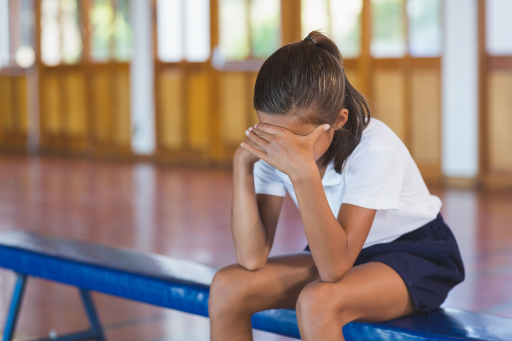 Sad schoolgirl sitting alone in basketball court at school gym, sexual harassment in school