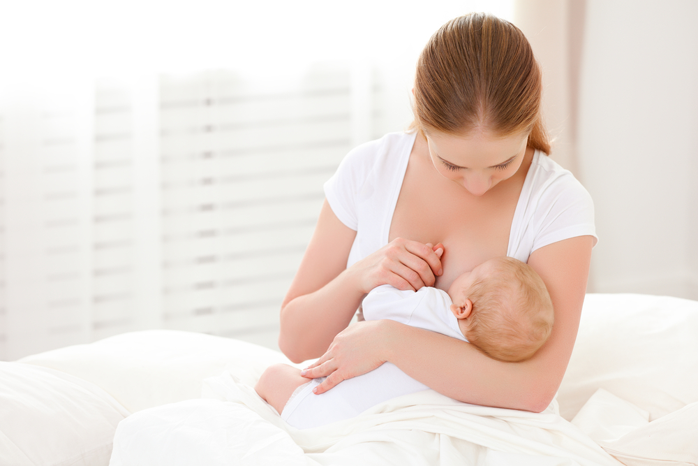 mother breastfeeding her newborn baby in a white bed