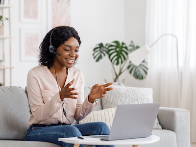 Video Conference. Smiling african woman having web call on laptop at home, talking at camera while sitting on sofa in living room, flexible working