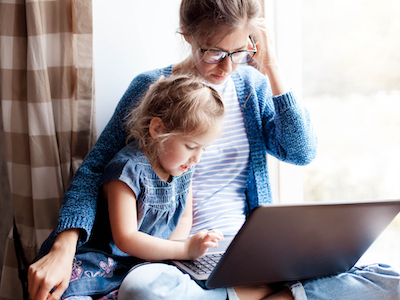 Working mom works from home office with kid. Mother and daughter read news. Woman and cute child sitting on window sill.