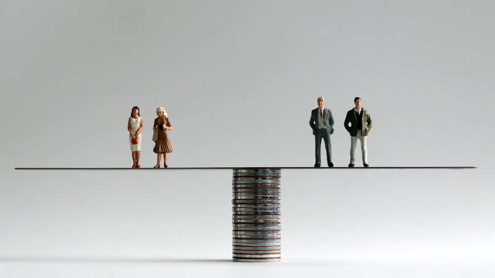 A group of miniature men and women standing on either side of a pile of coins, equal pay, gender pay gap