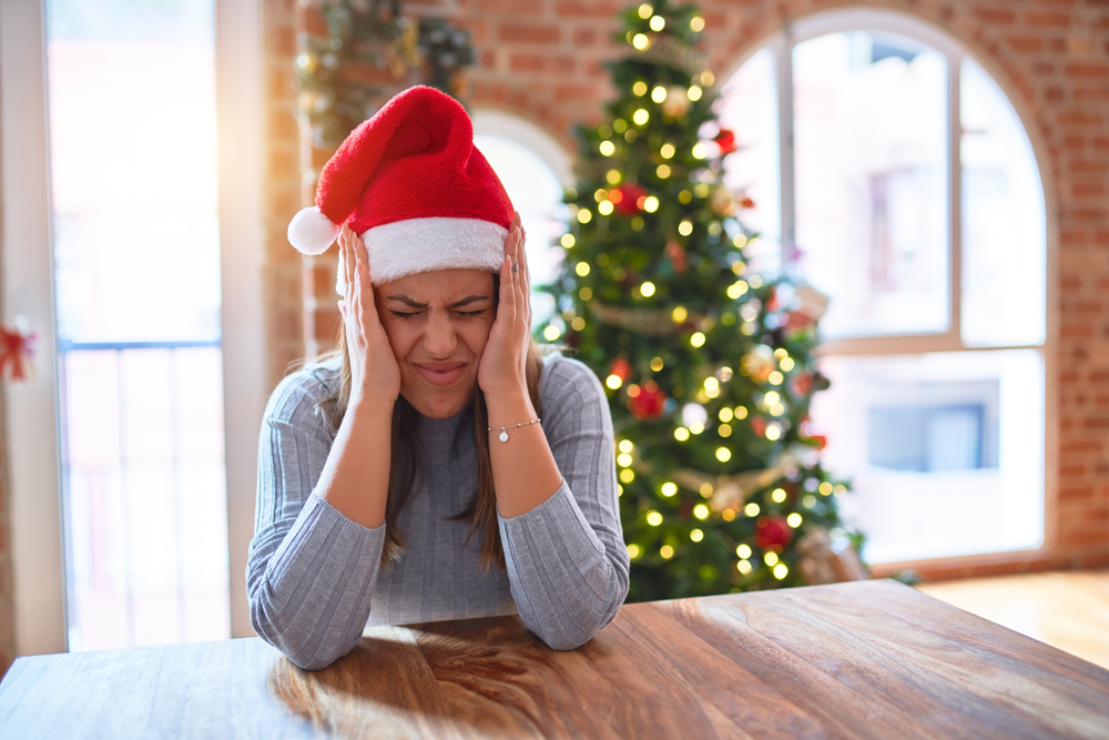 Young beautiful woman wearing santa claus hat at the table at home around christmas decoration suffering from headache desperate and stressed because pain and migraine.