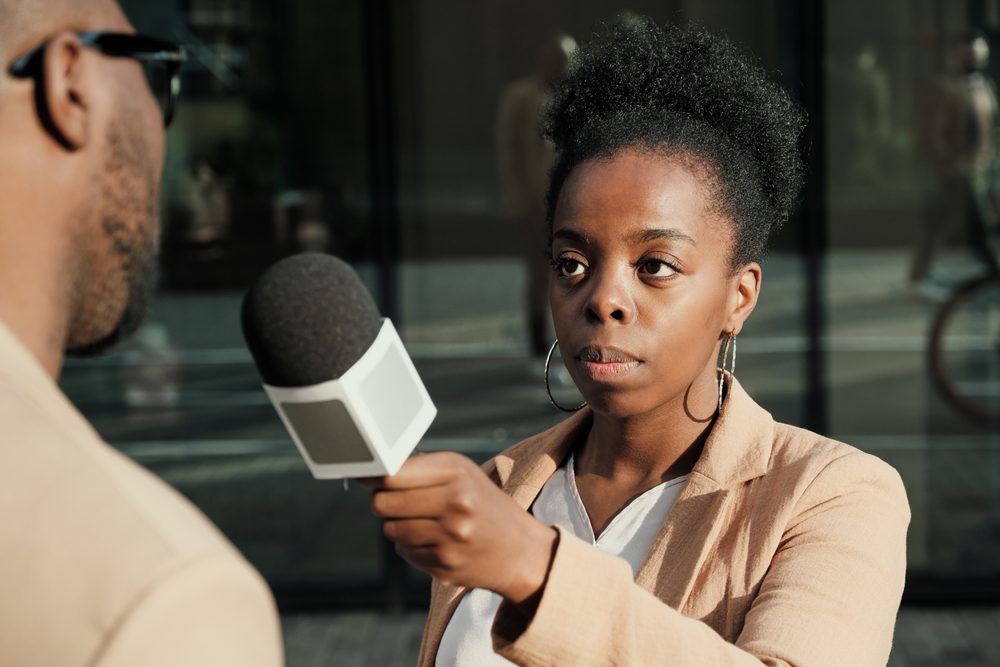 African female journalist holding microphone and interviewing the man outdoors, journalism