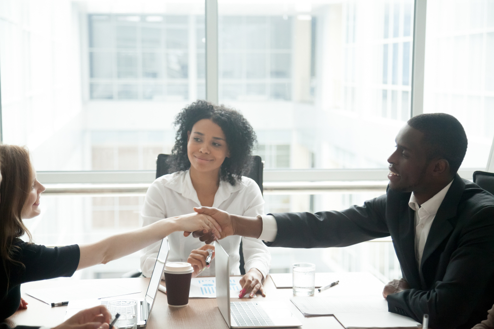 Smiling african businessman handshaking greeting caucasian businesswoman at group meeting negotiation, black satisfied entrepreneur welcoming partner shaking hand in lawyers office, respect concept, mediator