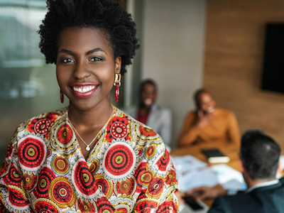 close up of beautiful young smiling professional black african business woman, coworkers hold a meeting in background, black female founders list
