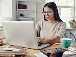 Beautiful young woman in casual clothing using laptop and smiling while working indoors