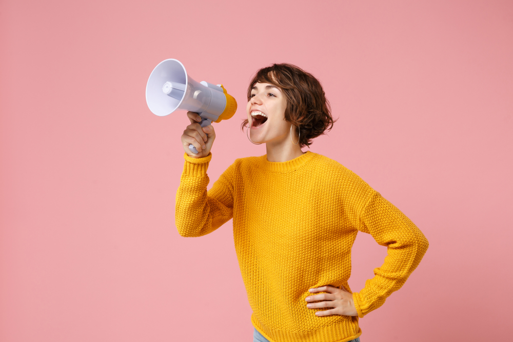 woman in a yellow jumper using a megaphone to get her voice heard