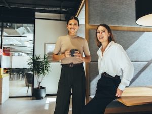 Cheerful female entrepreneurs smiling at the camera while standing in a modern co-working space