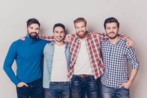 Diversity of men. Four cheerful young guys are standing and embracing, smiling, on pure background in casual outfit and jeans