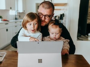 Man sitting at desk with his children, working from home, working parent, International men's day, working father