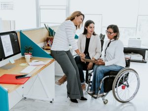 Disabled businesswoman in wheelchair and her female coworkers planning while working at corporate office.