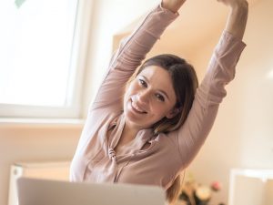 Happy woman sitting at desk performing yoga exercises, stretches