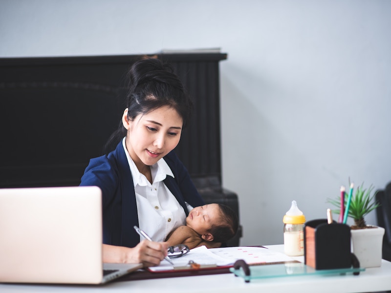 Working mother working at desk with newborn baby, juggling work and motherhood