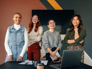 Successful female entrepreneurs smiling cheerfully while standing behind a table in a boardroom. Group of multicultural businesswomen working together in a modern office.