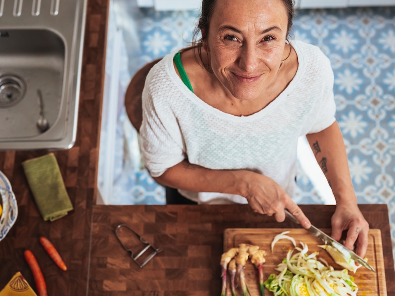 Smiling woman in kitchen, cutting vegetables, menopause, restoring balance